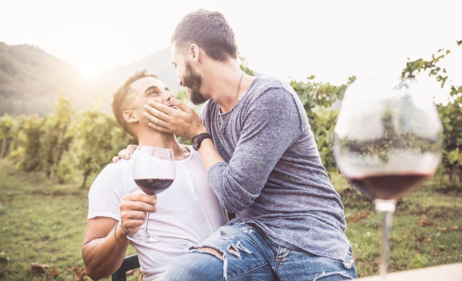 Two men kissing at a vineyard during a gay event, enjoying a glass of wine.