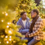 Two people sitting in front of a Christmas tree at local gay events.