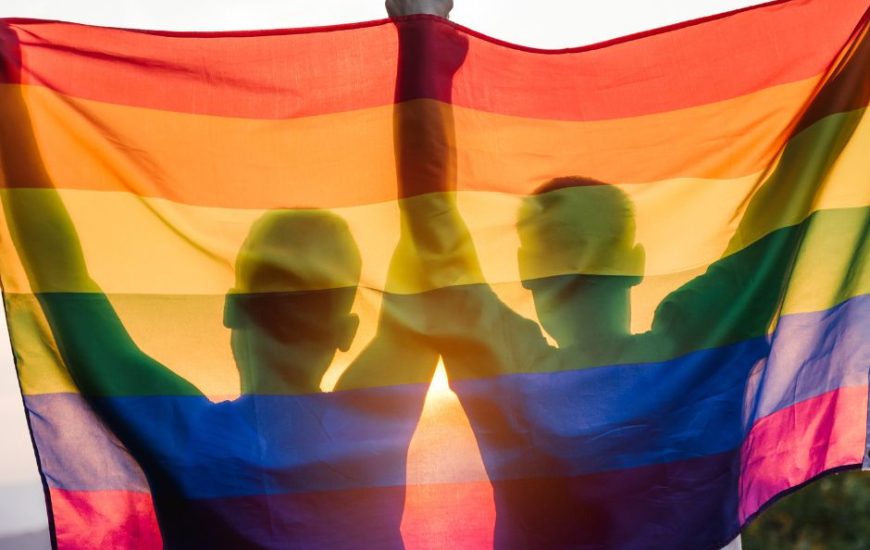 Two men, proud participants of gay events on the Sunshine Coast, are holding up a rainbow flag.