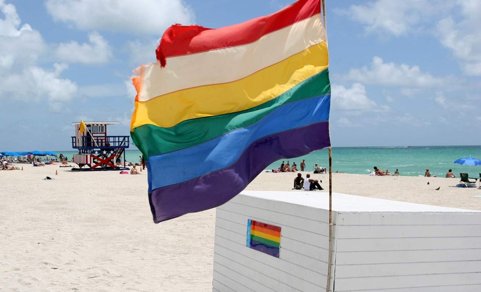 A rainbow flag is fluttering on the beach at a gay beach.