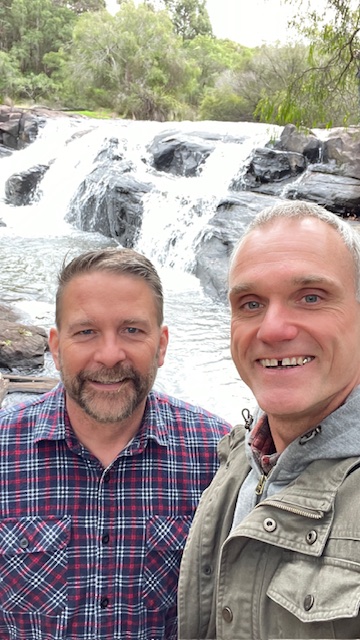 Two men standing in front of a waterfall at a gay event.