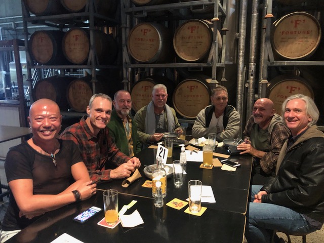 A group of men, possibly participants of local gay pride events, sitting at a table in a brewery.