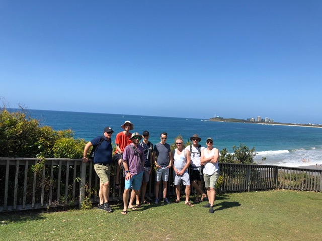 A group of people standing on a grassy area near the ocean, gathered for one of the gay events organised by QAF Tours and Events.
