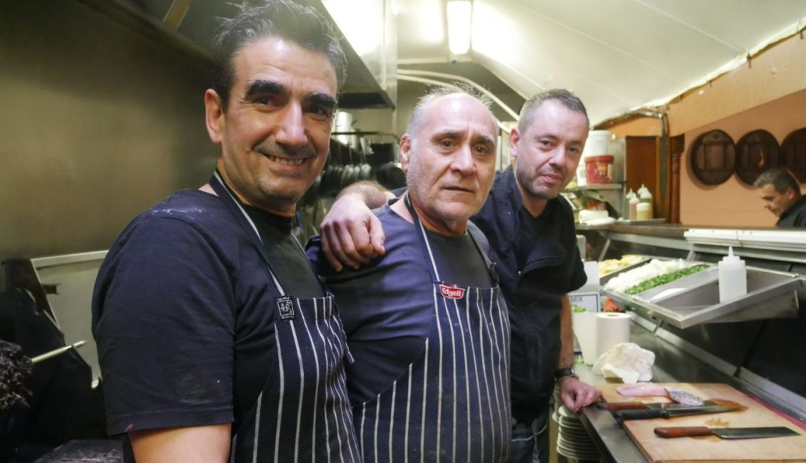 Three men at a gay event posing for a photo in a kitchen.
